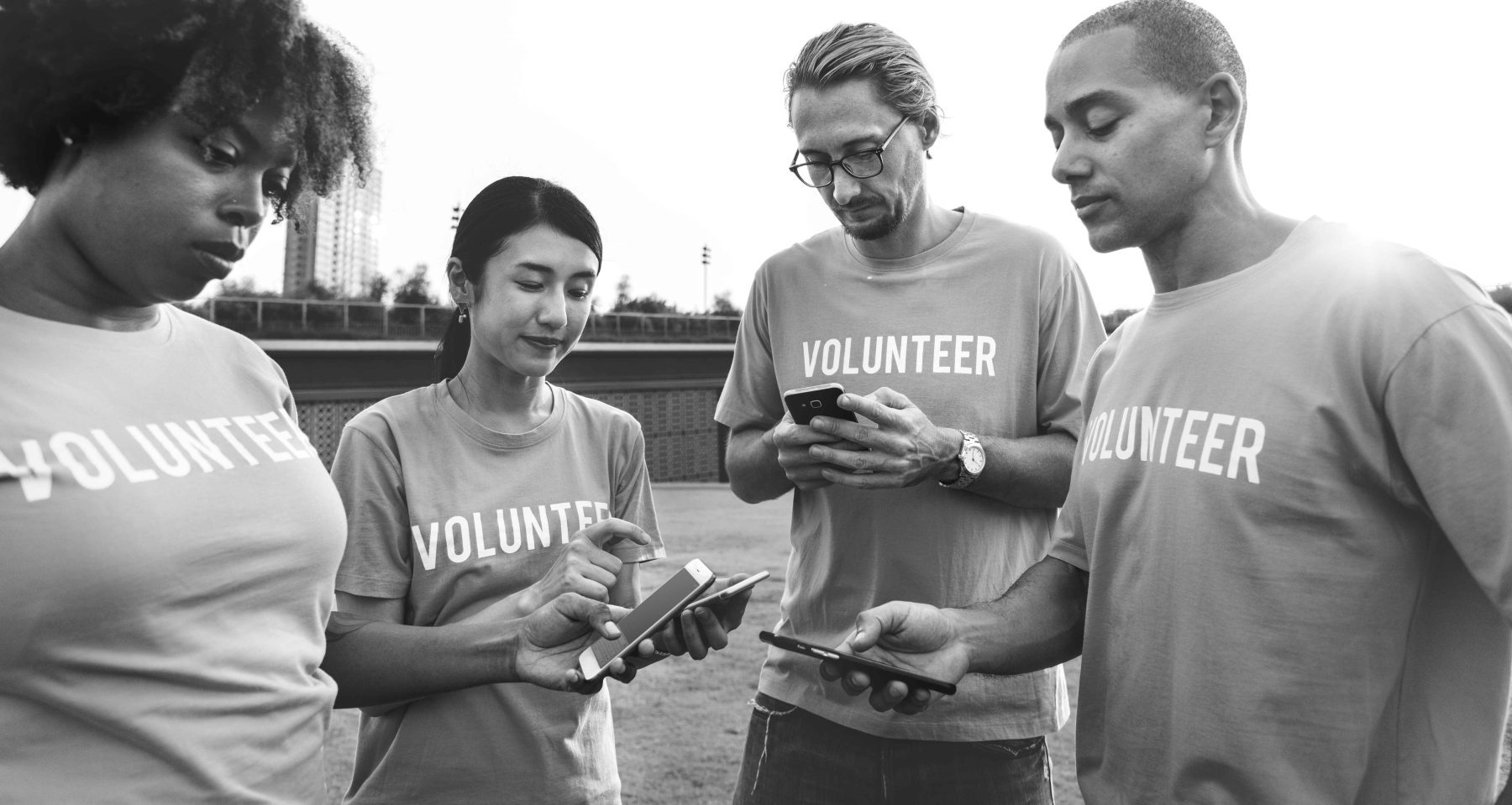 Four volunteers collaborating while posting updates on social media using a smartphone