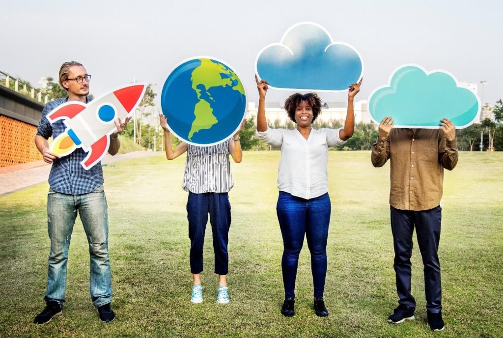 Four diverse individuals holding internet-related icons — a rocket, Earth, and cloud symbols — while standing on grass, representing digital access and connectivity for nonprofits and community organizations exploring affordable internet plans.